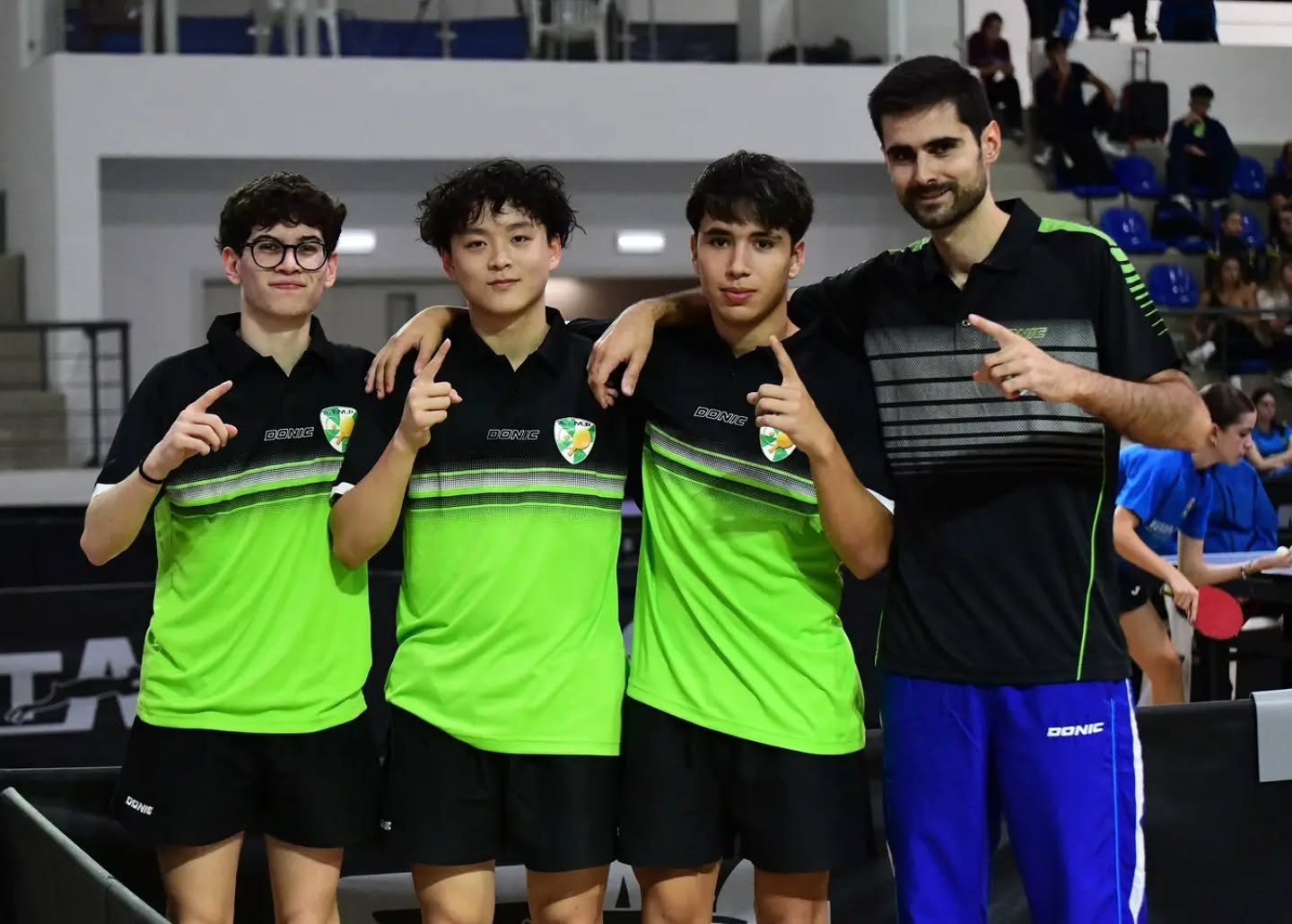 Quatro pessoas ligadas à equipa do Guilhabreu posam num pavilhão de ténis de mesa, três com camisolas pretas e verdes.